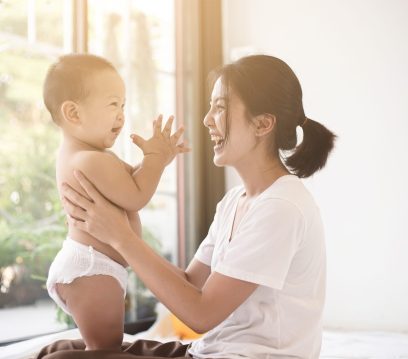 Asian mom smiling happy holding and playing with her son in living room. Mom and baby clap your hands together. Mom and baby in mother’s day concept.